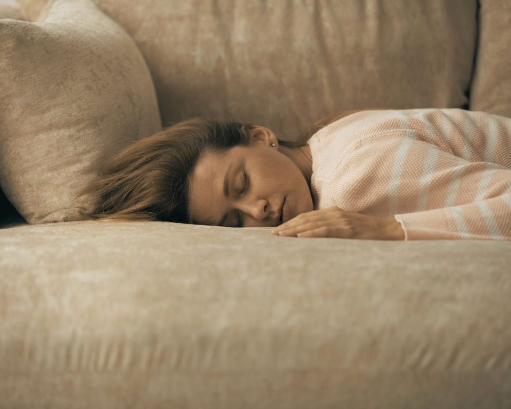 Femme allongée et endormie sur un canapé beige, suggérant fatigue, épuisement ou besoin de récupération.